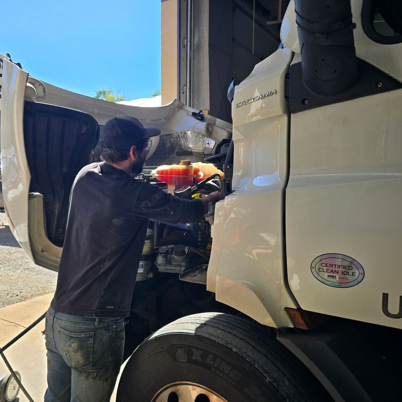 Technician servicing the engine bay of a Freightliner Cascadia